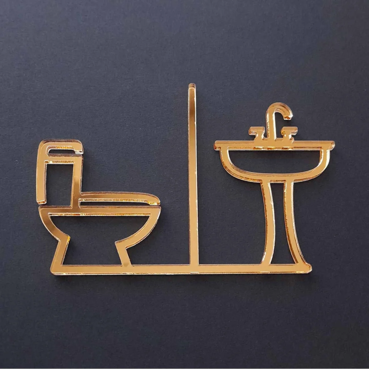 Zlatý zrkadlový piktogram na označenie dverí zložený zo symbolu toalety WC a umývadla